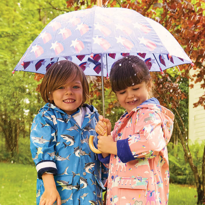 two kids wearing raincoats holding umbrella