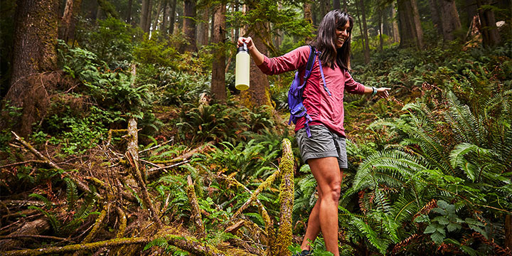 woman walking in a forest with arms open and Hydro Flask in hand