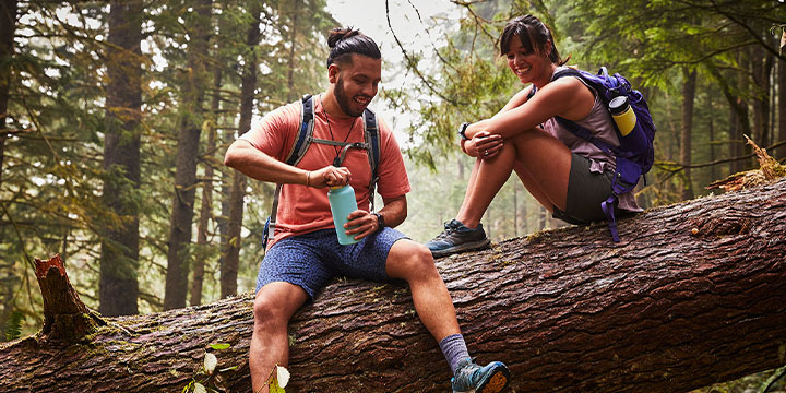 man and woman sitting on a tree log with Hydro Flask in his hands