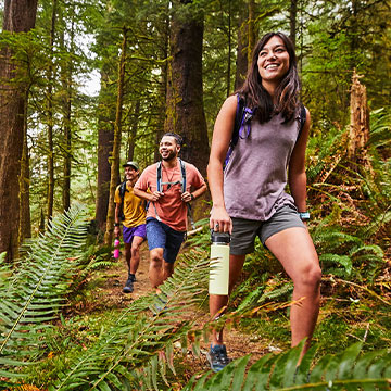 three people hiking in forest and woman holing a Hydro Flask bottle