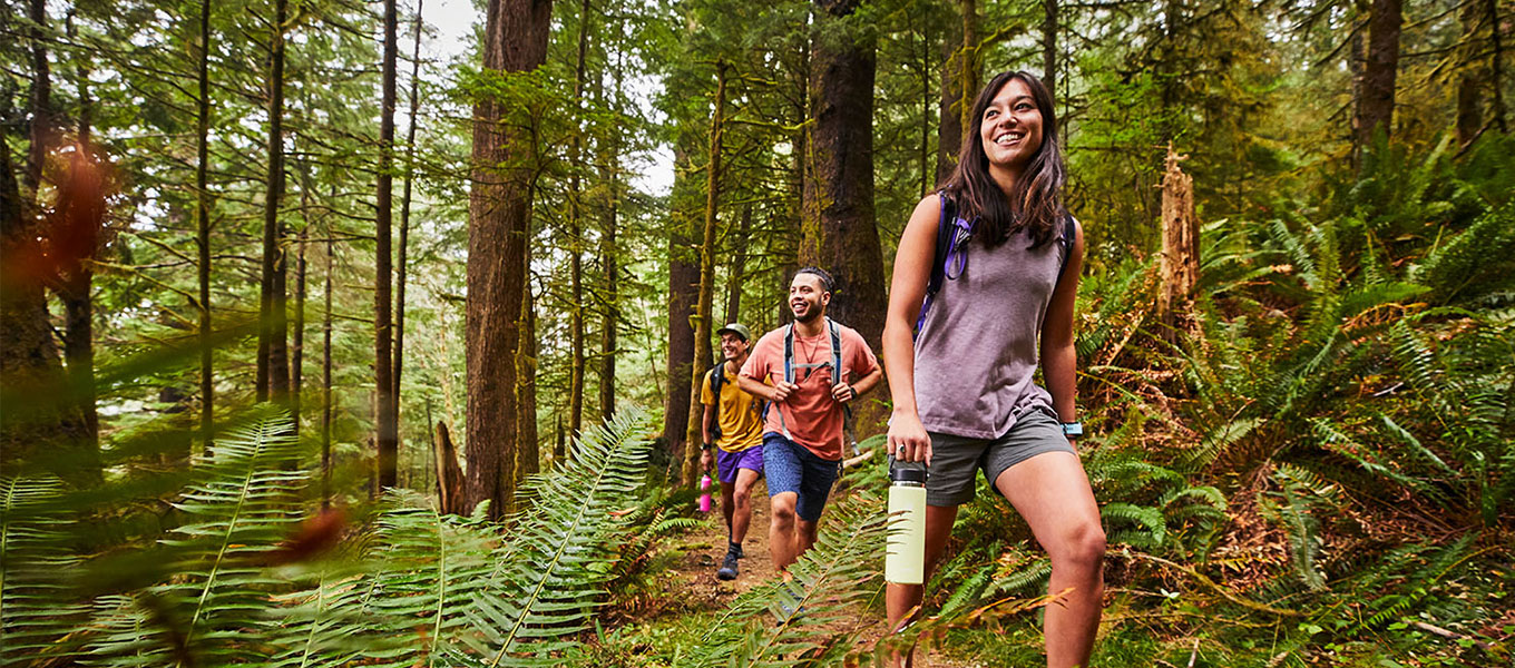 three people hiking in forest and woman holing a Hydro Flask bottle
