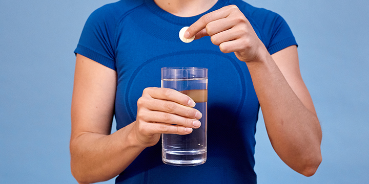 woman holding glass of water and nuun tablet